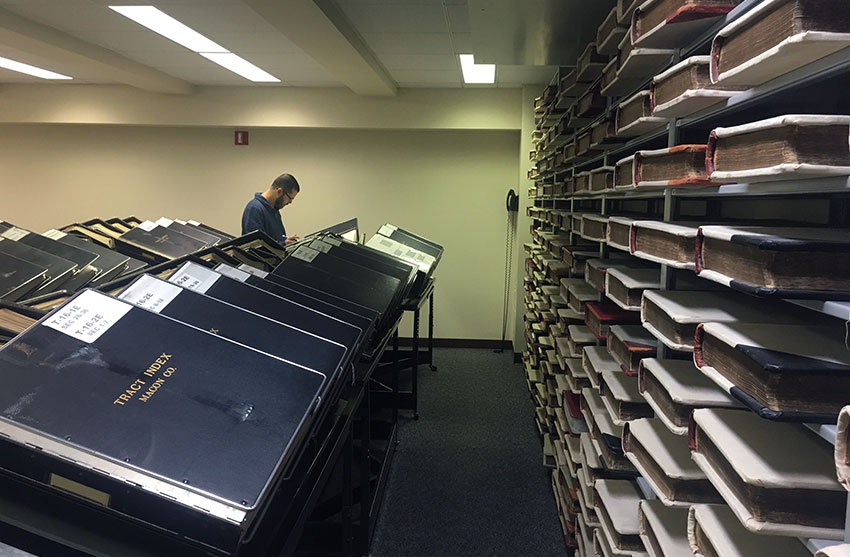 Room full of binders of records with a man in the background reading through one binder
